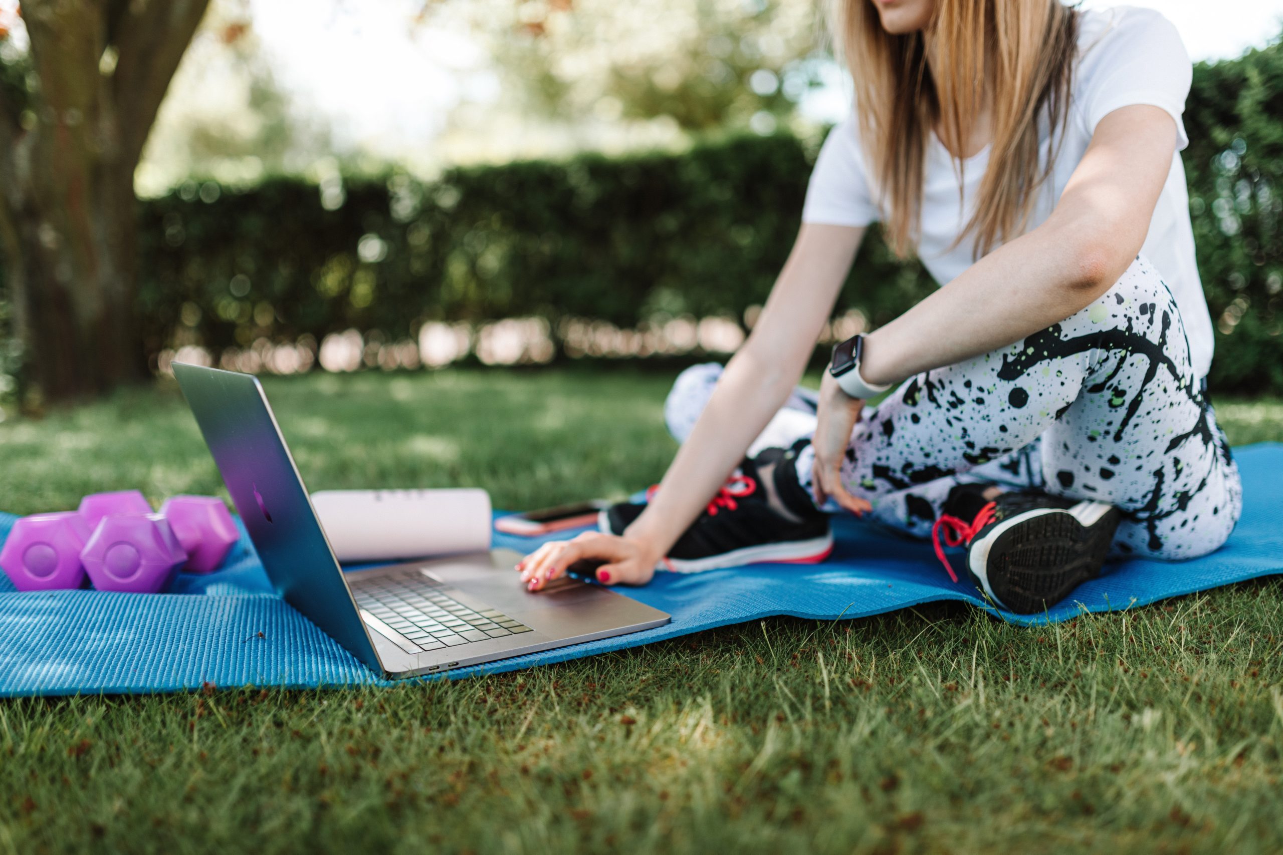 Shallow focus photo of a woman in activewear using a laptop while sitting on a yoga mat