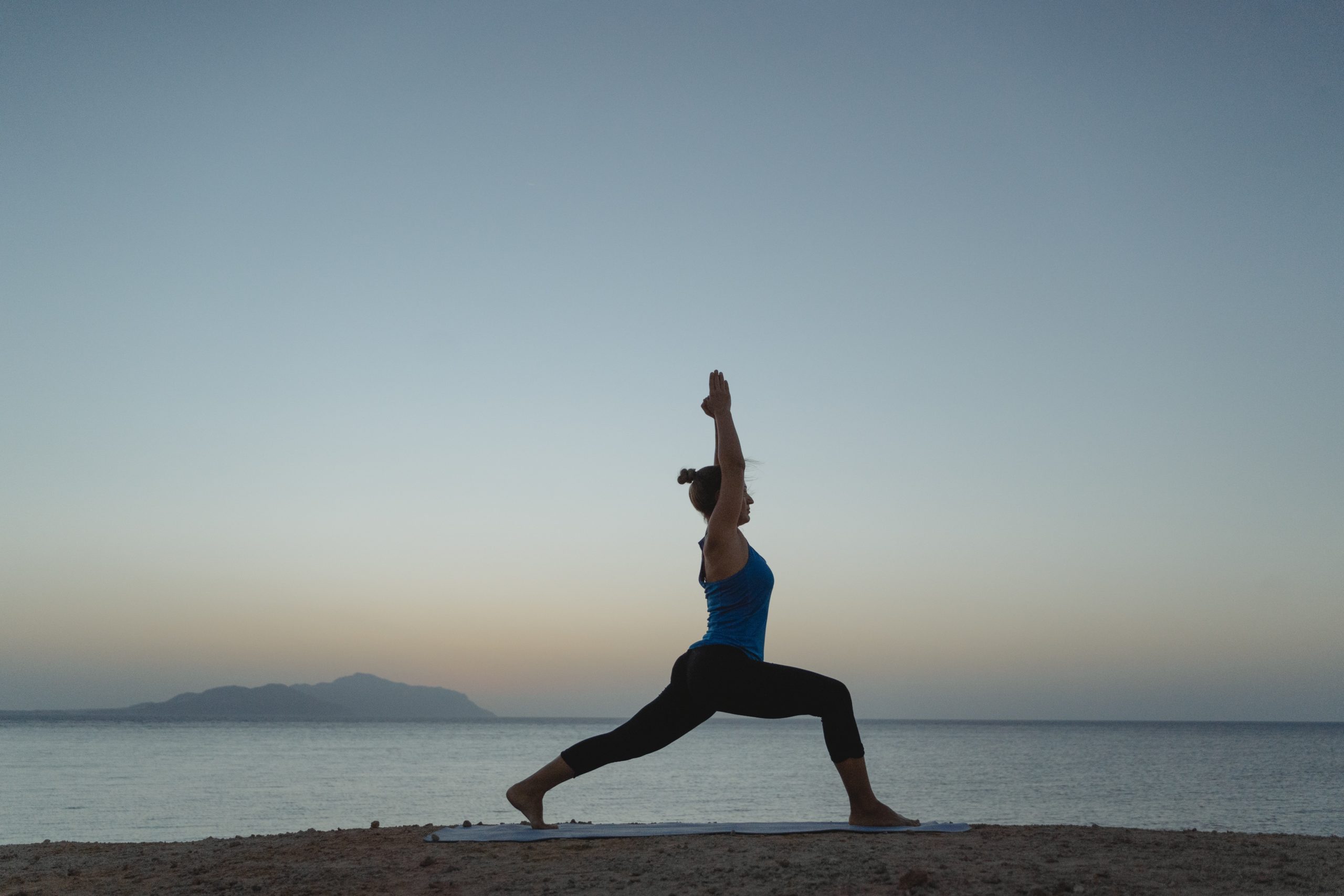 Woman standing in yoga pose on beach shore during sunset