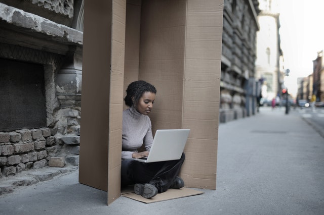 A woman sitting inside a cardboard box with a laptop.