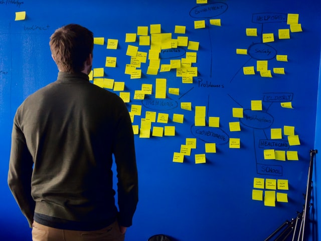 Man starting at a blue board covered with yellow Post-it notes related to problems