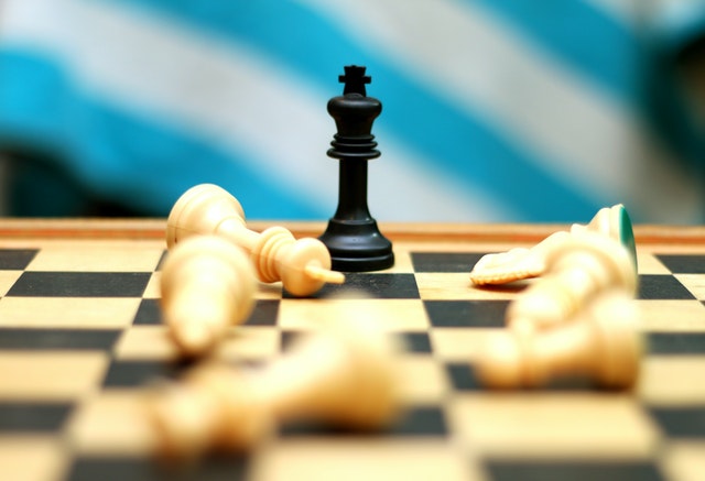 Close up of black king chess piece taking down white pieces on a chessboard.