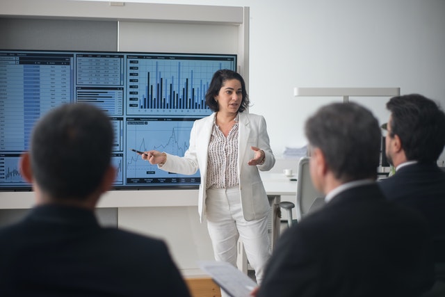 A woman presenting to a group at an office with the help of financial graphs