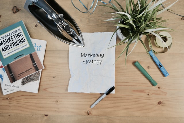 Marketing strategy written on a white paper on the table with a plant and pens around.