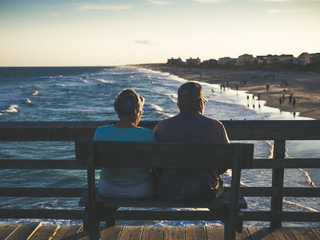 Two people sitting on a bench facing the ocean.