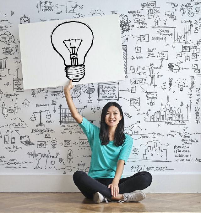 A woman holds a whiteboard with a lightbulb drawn on it.