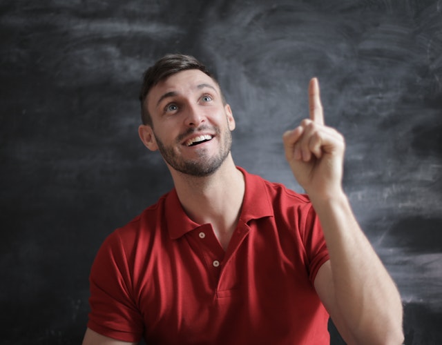 A man in a red polo shirt gesturing that he is thinking of a good idea.