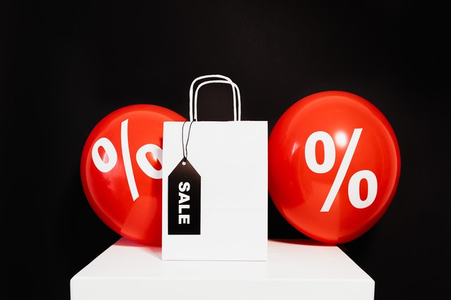 A white paper bag labeled “sale” between red balloons with percentage symbols