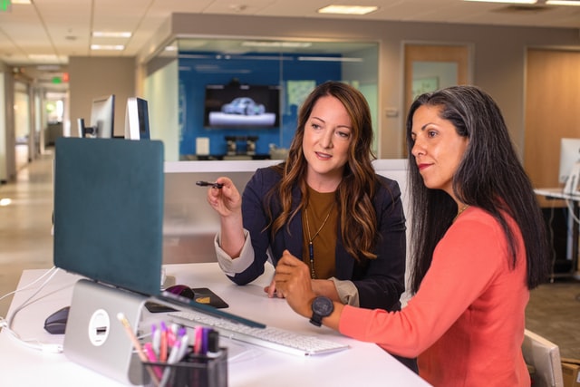 Two businesswomen talking about Finance in office at a desk with a laptop