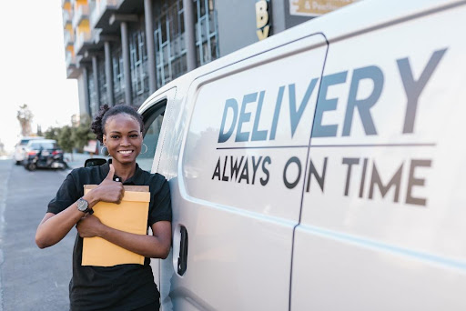 Woman in black shirt giving a thumbs-up while standing beside a delivery van